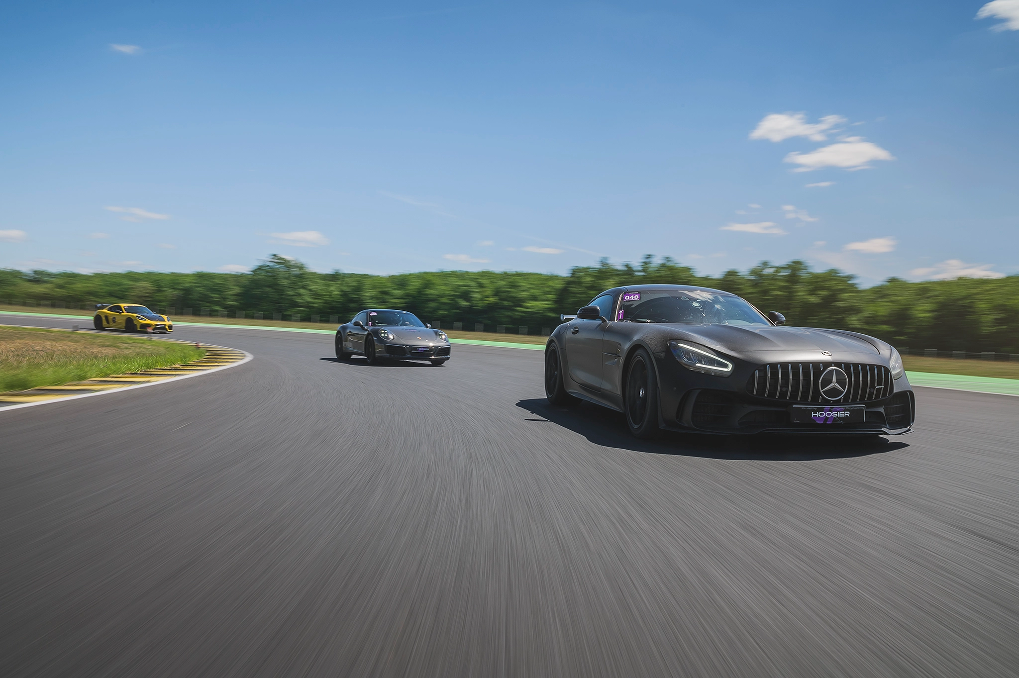 Three cars cornering together on track, yellow, grey and black
