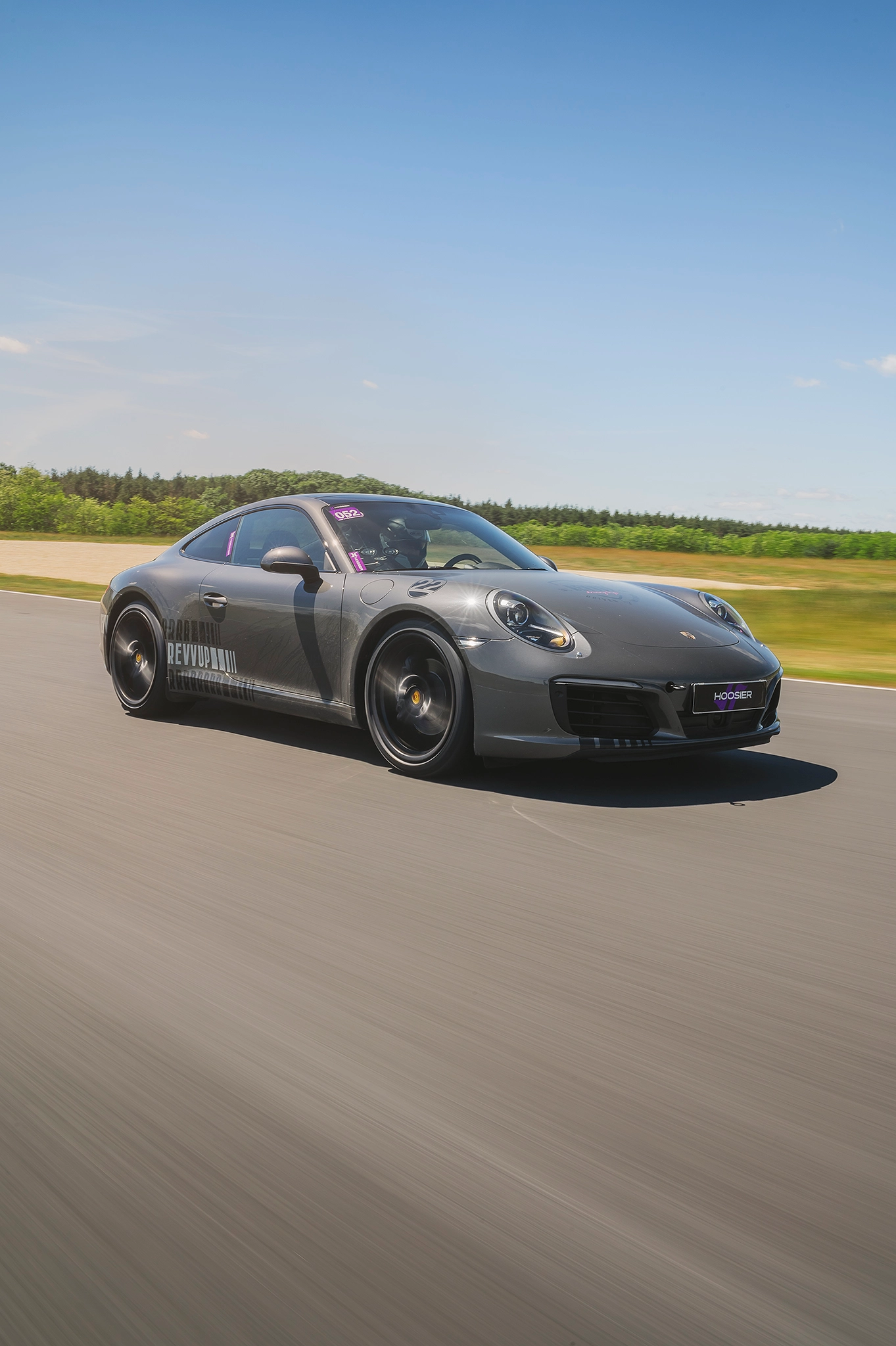 Porsche 911 on track at speed, driver visible through windshield